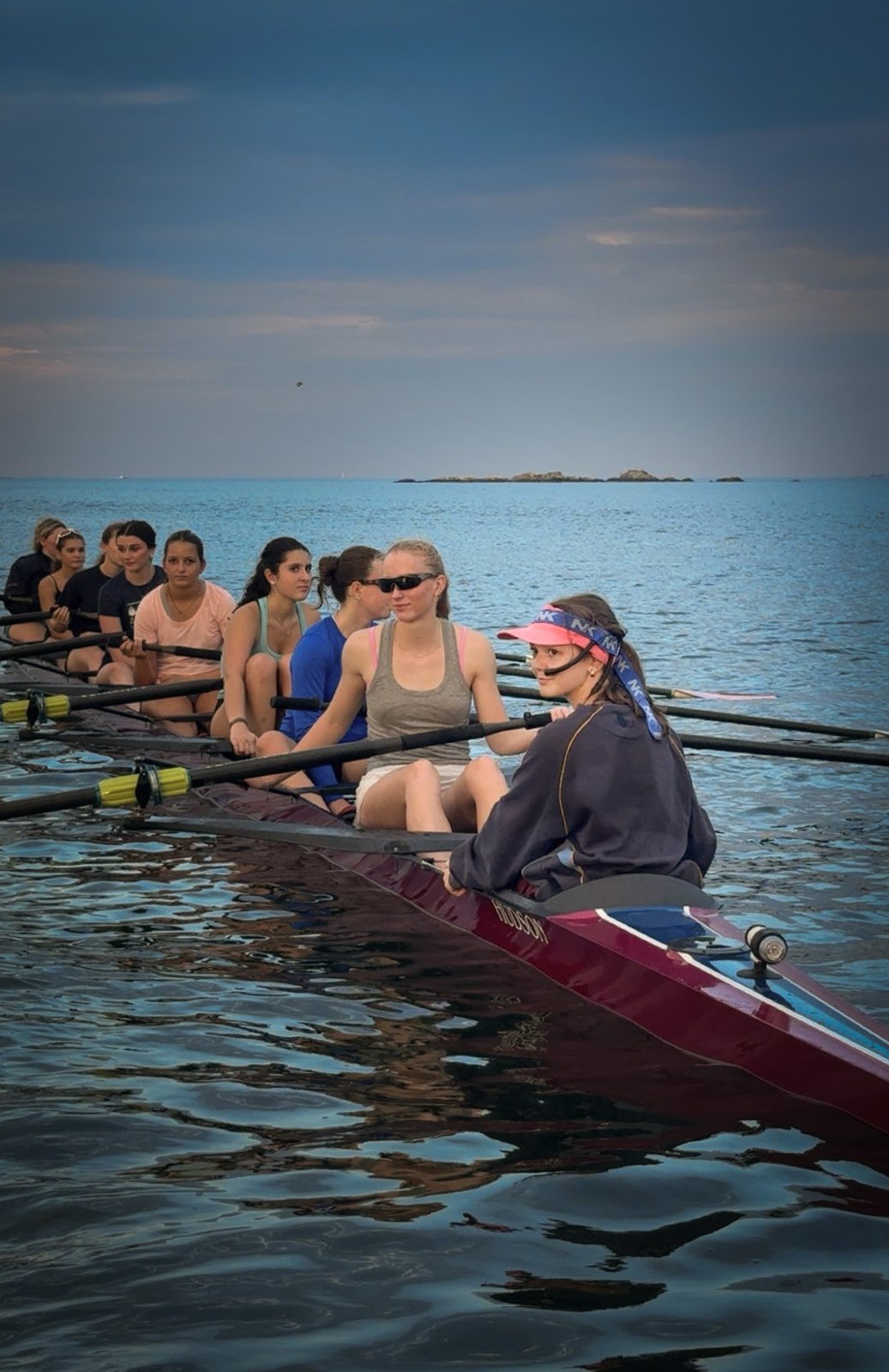 A coxswain looking back from the stern of a boat, crew behind her